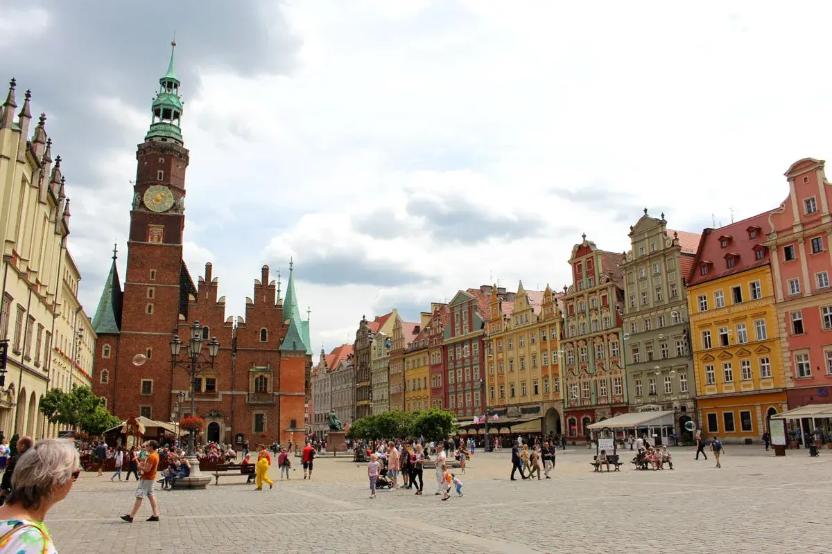 Buntes Treiben auf dem Marktplatz der Breslau Innenstadt. Das Rathaus mit seinem markanten Turm dominiert die Szene, umgeben von farbenfrohen Bürgerhäusern.
