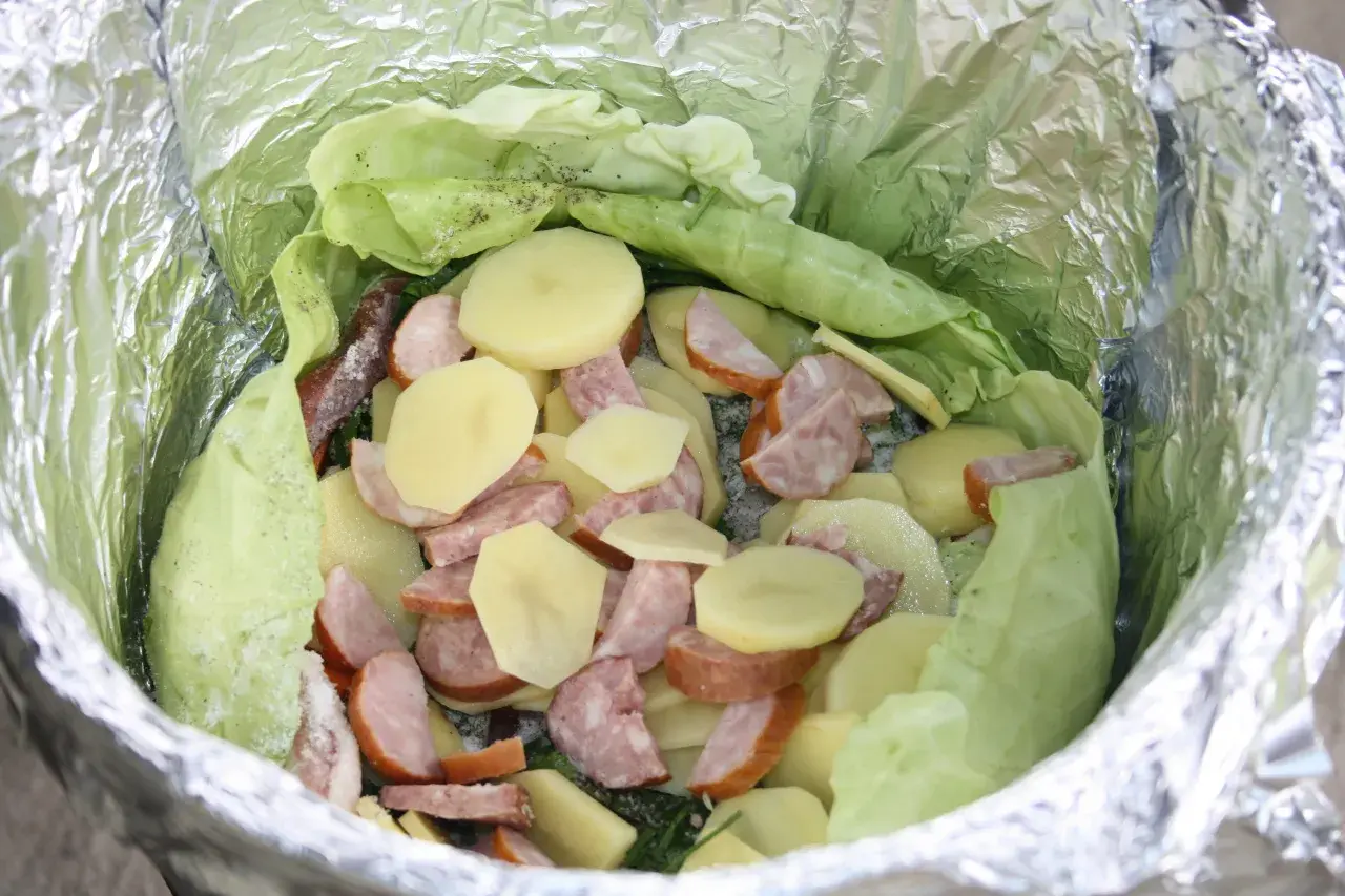 Gotowe dania na ognisko: ziemniaki, kiełbasa i kapusta zawinięte w folię aluminiową, czekają na pieczenie.