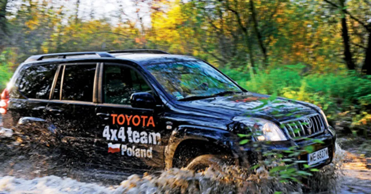 Czarny Toyota Land Cruiser 100 z napisem "4x4 team Poland" pokonuje błotnistą trasę w lesie.