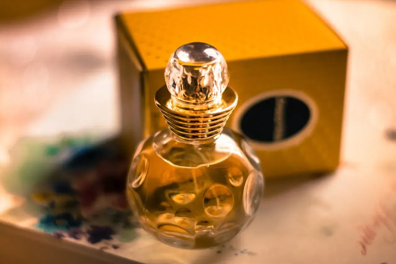 Złota buteleczka perfum Christian Dior Dolce Vita z kryształowym korkiem, obok żółtego pudełka.