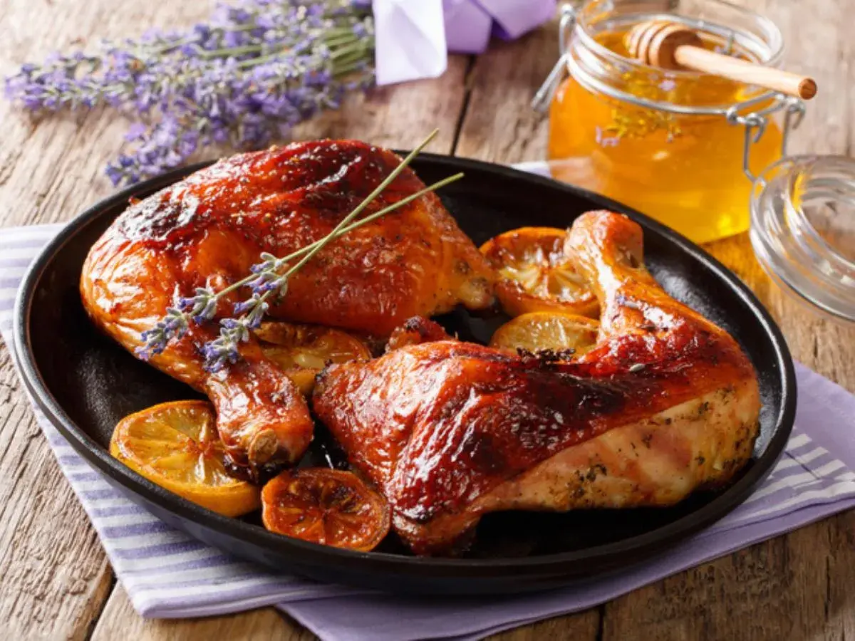 Muslos de pollo al horno dorados y jugosos, servidos con rodajas de limón y un toque de lavanda. Un tarro de miel dorada acompaña este delicioso plato.