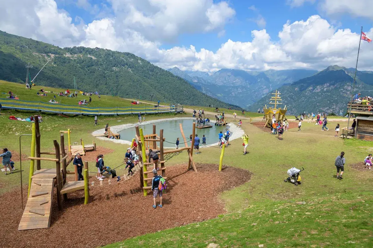 Un'area giochi con un laghetto e un galeone, dove tante famiglie si divertono in montagna con i bambini.