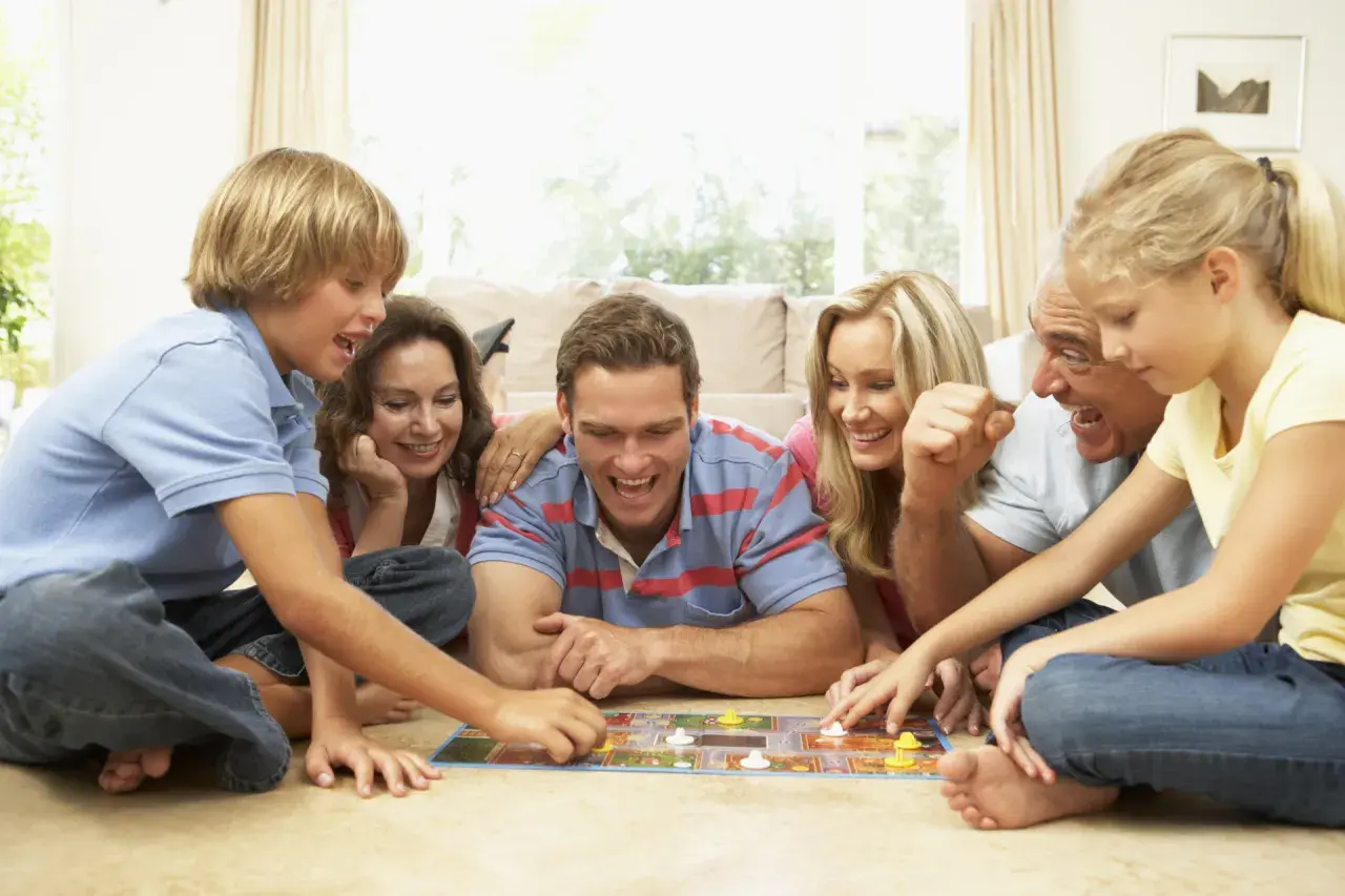 Familie spielt ein kooperatives Brettspiel, lachend und konzentriert auf dem Boden liegend.