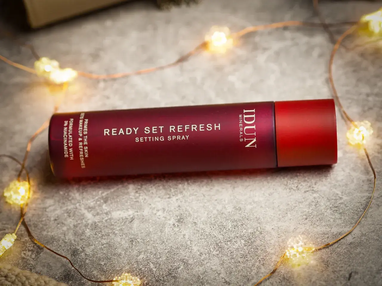 En röd flaska med IDUN Minerals Ready Set Refresh Setting Spray ligger bland julbelysning.