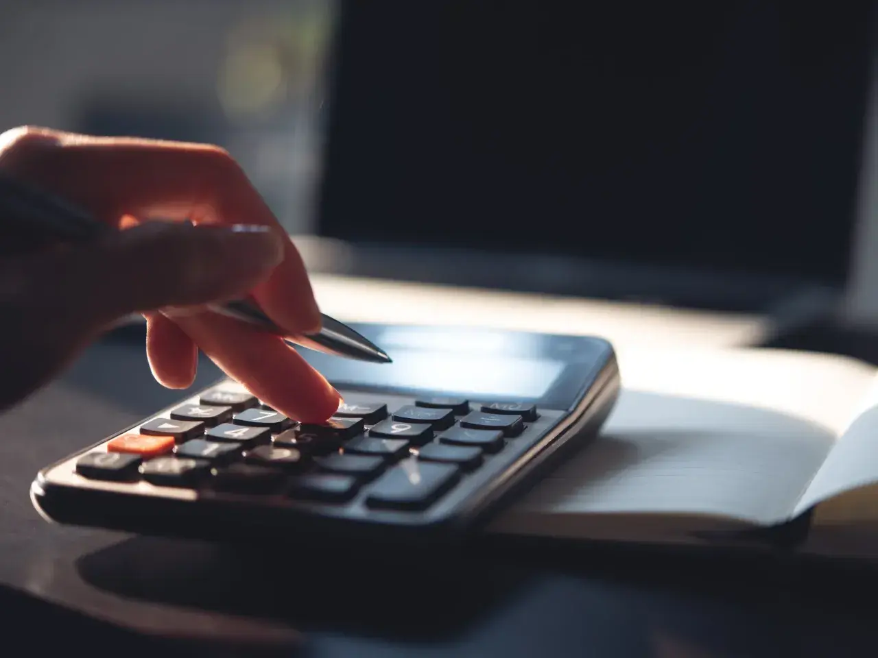 Dłoń z długopisem naciska klawisze kalkulatora, licząc, ile zarabia 1% najbogatszych Polaków. Obok leży otwarty notatnik i laptop.