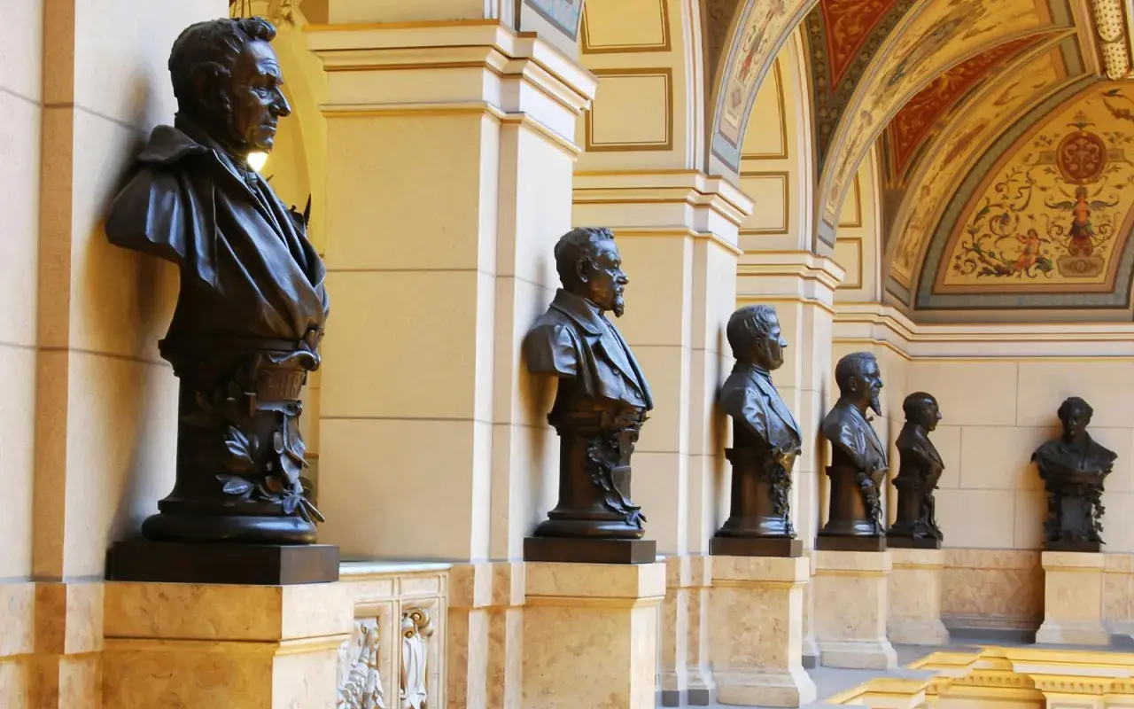 Büsten von Männern im Nationalmuseum Prag, flankiert von Säulen und einer reich verzierten Decke.