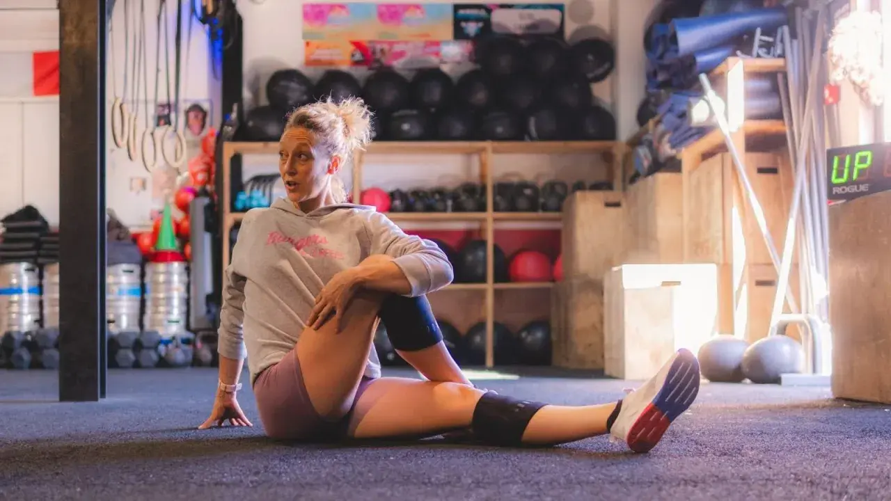 Femme en tenue de sport s'étirant au sol, profitant des bienfaits des étirements dans une salle de sport.