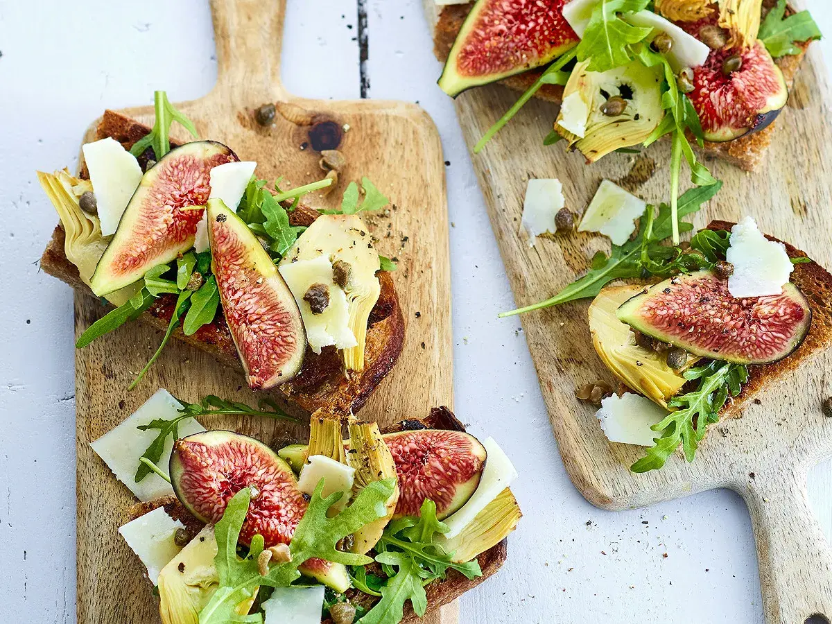 Tartines de pain grillé garnies de figues fraîches, d'artichauts, de roquette et de copeaux de parmesan.
