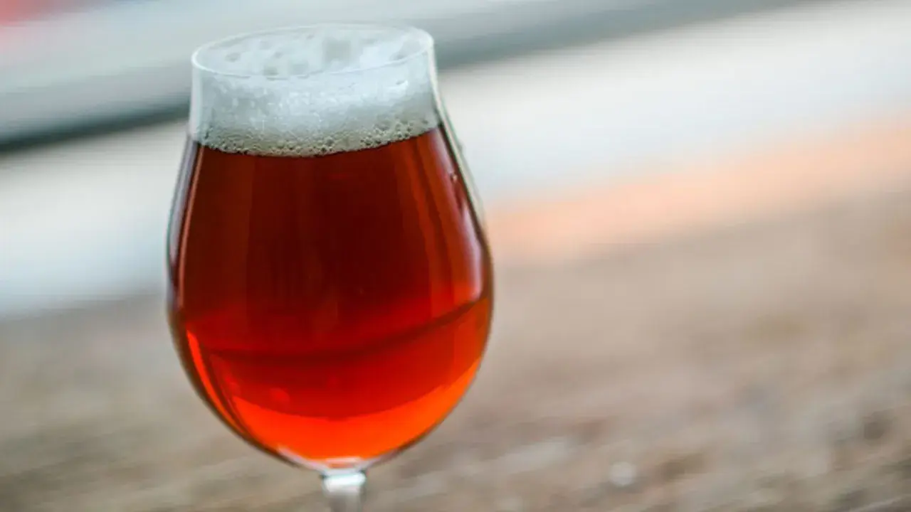 Un bicchiere di irish red ale con schiuma bianca, su un tavolo di legno.