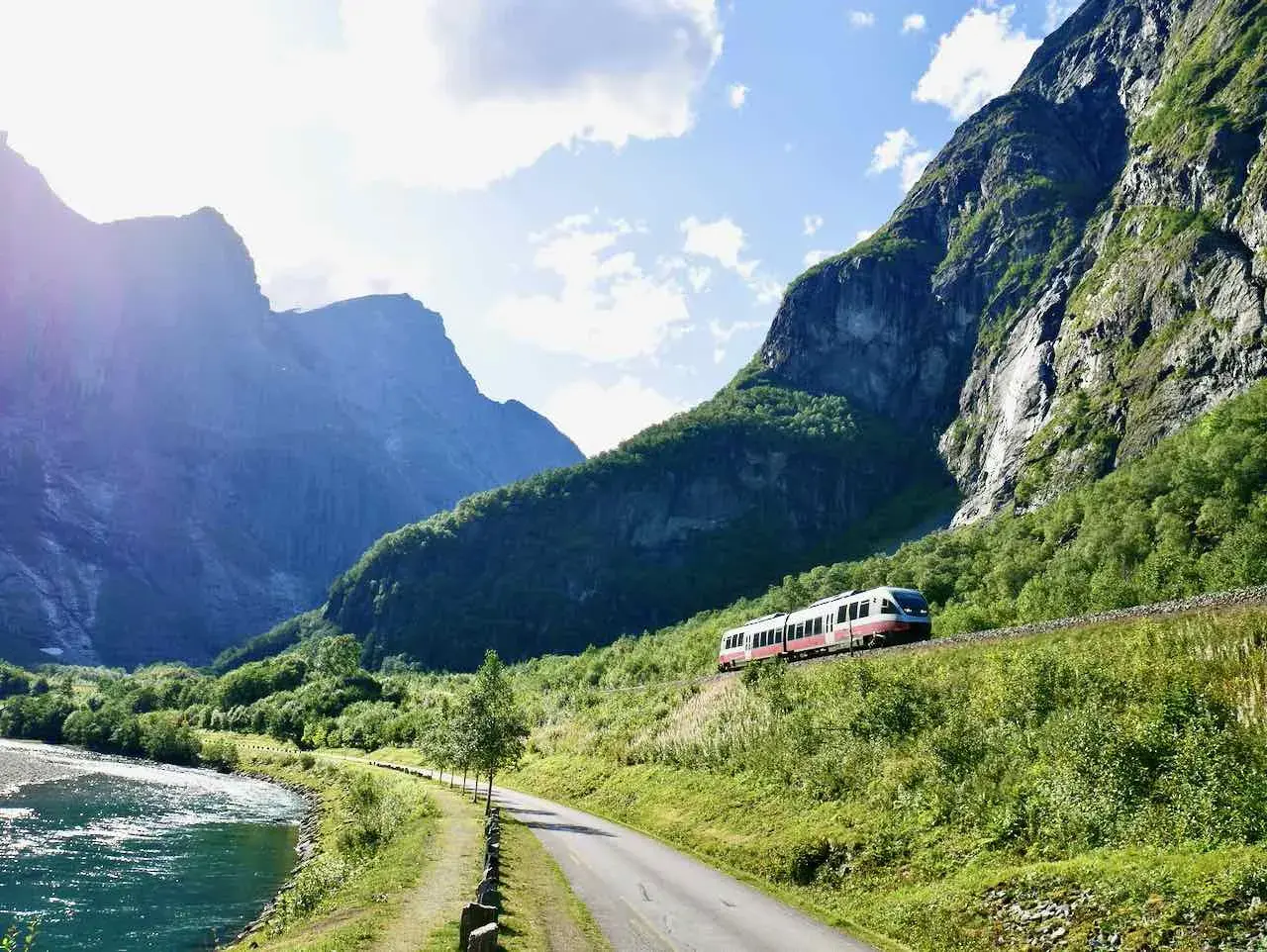 Ein Zug fährt durch eine malerische Berglandschaft. Ein perfekter Urlaub mit dem Zug, vorbei an einem Fluss und grünen Hängen.