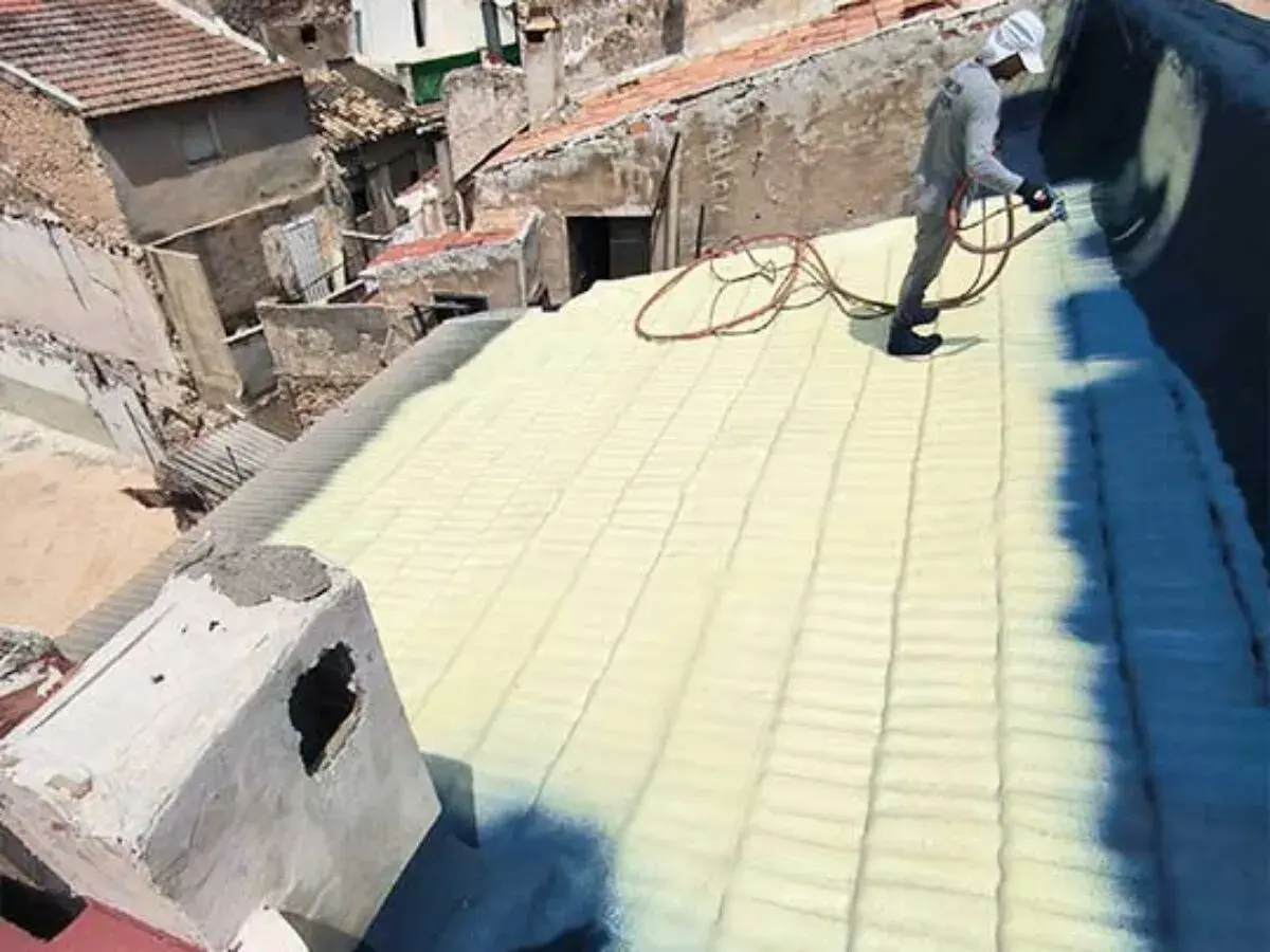Trabajador aplica aislamiento con poliuretano en un tejado. La espuma amarilla cubre las tejas, creando una capa protectora.