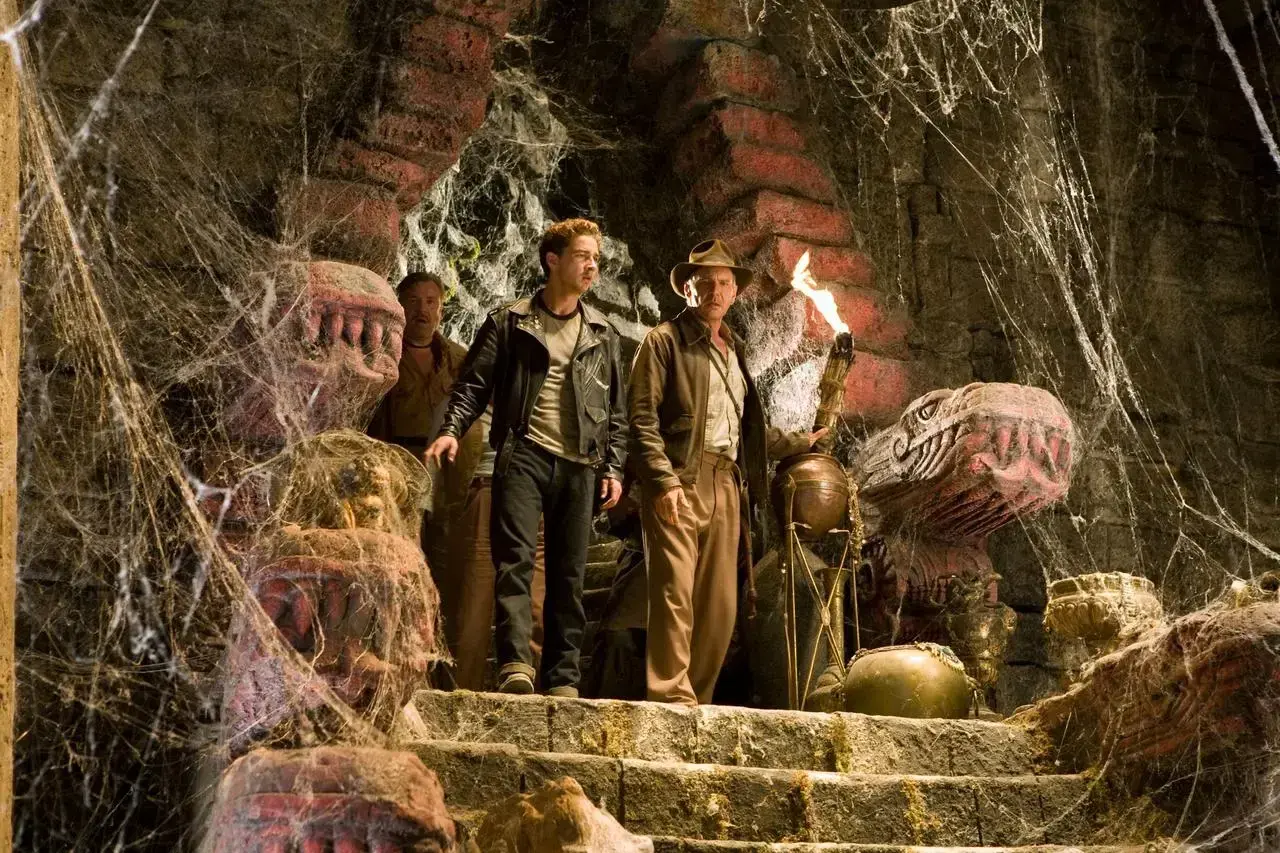 Indiana Jones i Królestwo Kryształowej Czaszki obsada: Indiana z pochodnią i Mutt na schodach w pajęczynach, obok kamiennych głów.