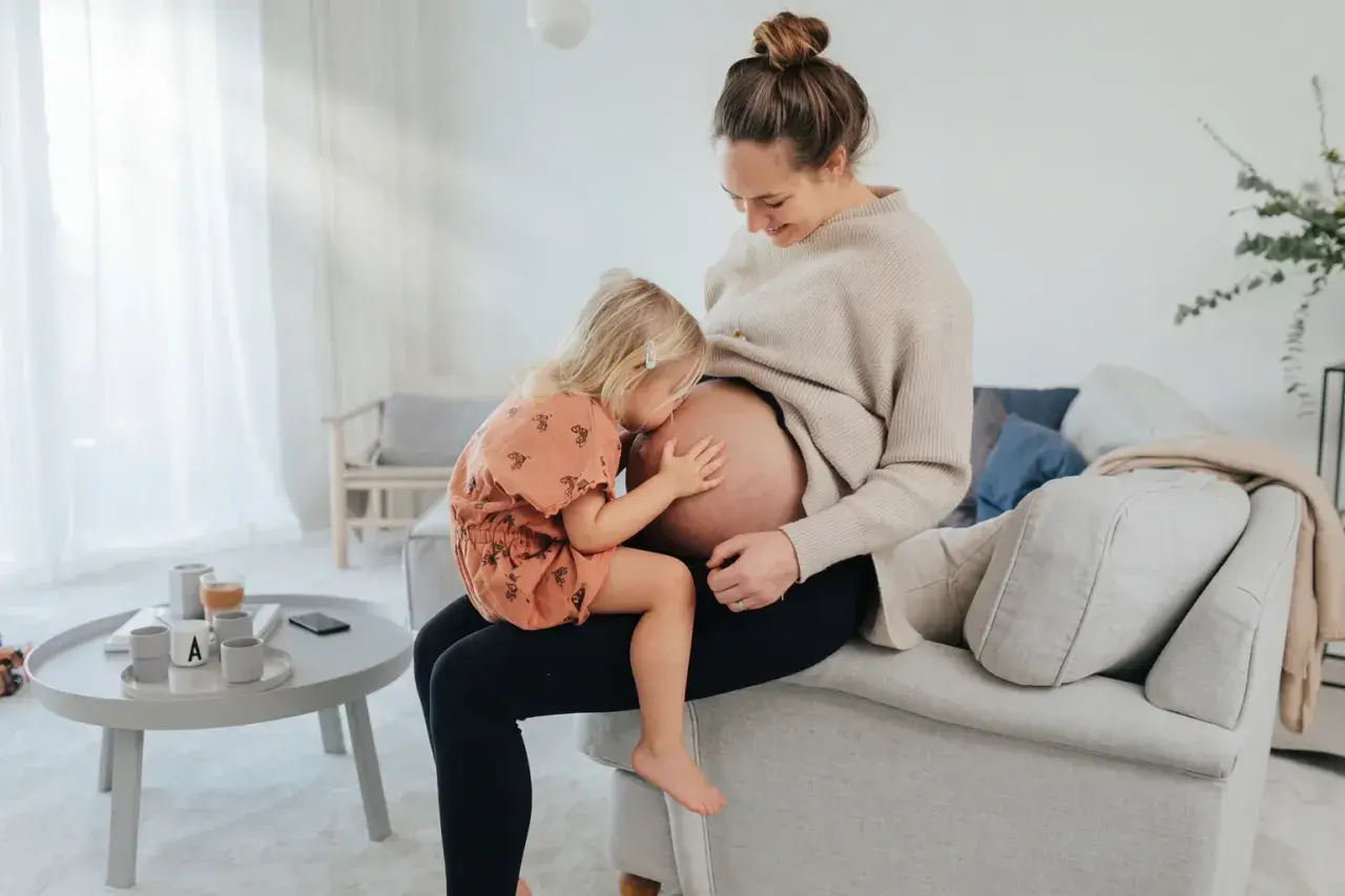 Liten flicka kramar sin mammas mage. En fin stund för en gravid kvinna som tar folsyra.