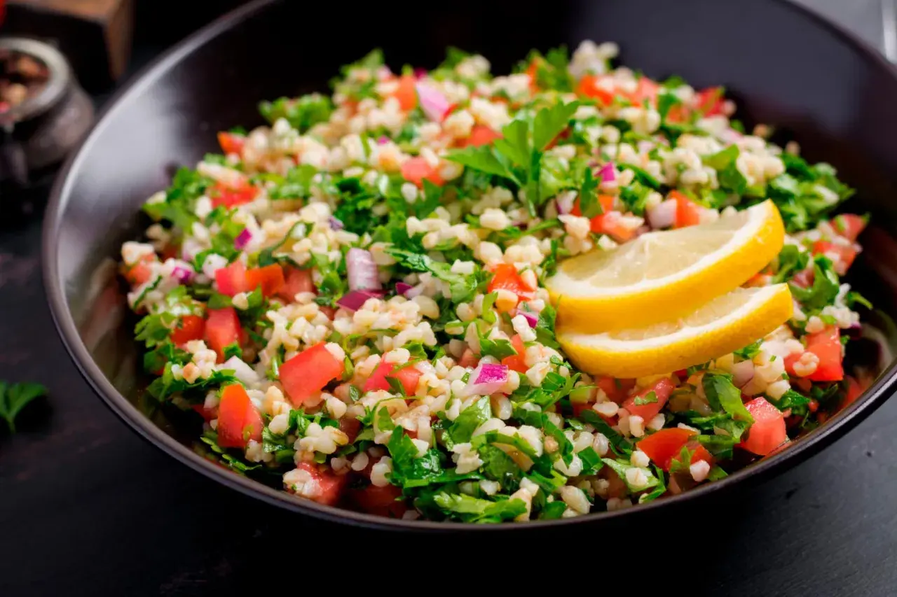Delicioso tabule receta, una ensalada fresca de bulgur, tomate, perejil y cebolla morada, adornada con rodajas de limón.
