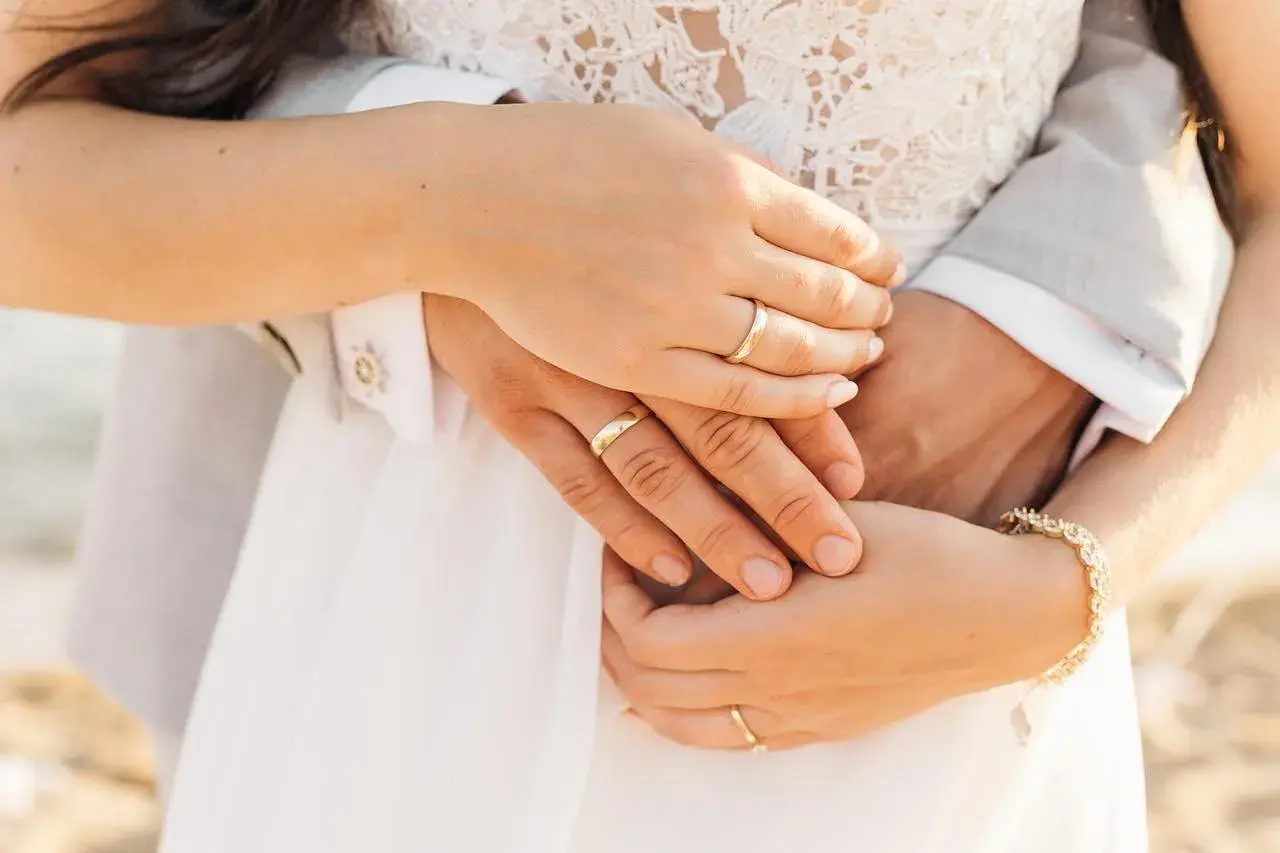 Manos entrelazadas con anillos de boda, mostrando dónde se pone el anillo de compromiso. Un detalle de amor eterno.