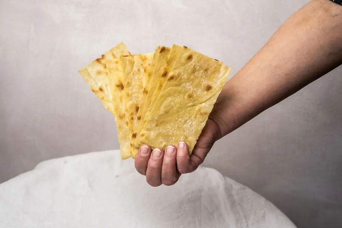 Mano sostiene varias láminas de pan carasau dorado y crujiente, con pequeñas manchas tostadas.