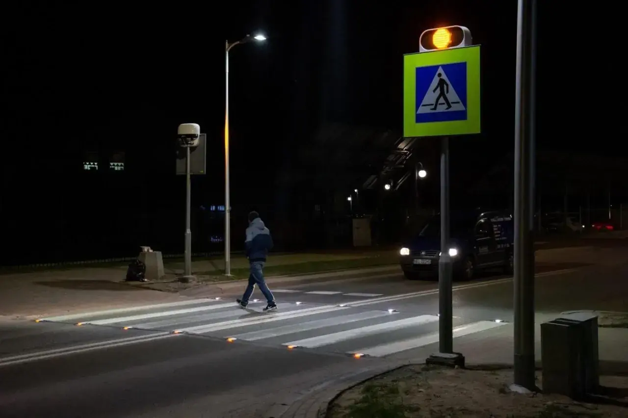 Nocą pieszy przechodzi przez pasy, oświetlone odblaskami. Obok miga żółte światło sygnalizatora, a znak d6 przypomina o obowiązku ustąpienia pierwszeństwa.