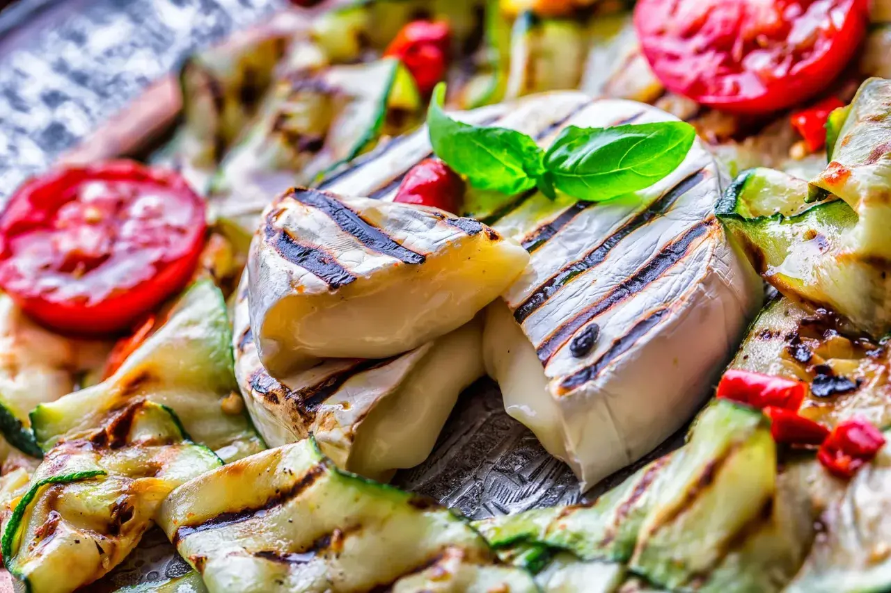 Co na grilla oprócz mięsa? Grillowany ser camembert z cukinią i pomidorami, udekorowany bazylią.