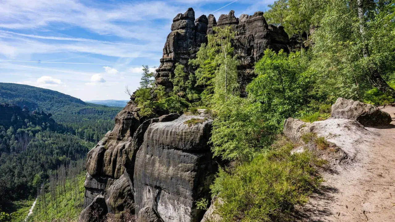 Felsformationen im Elbsandsteingebirge, ideal zum schmilka wandern. Ein Pfad führt durch üppige Vegetation zu den bizarren Felsen.