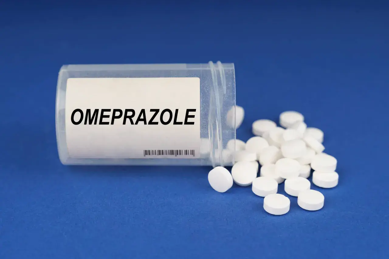 Białe tabletki z napisem OMEPRAZOLE rozsypane z pojemnika. Bioprazol pomaga w leczeniu dolegliwości żołądkowych.