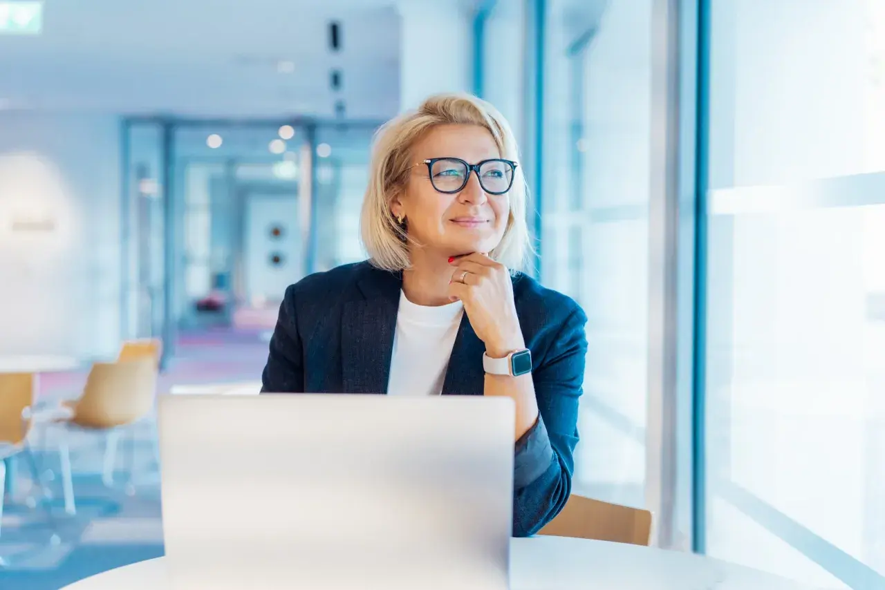 Donna bionda con occhiali, seduta al computer, pensa al suo futuro. Un nuovo capitolo, cambiare lavoro a 50 anni, è una possibilità concreta.