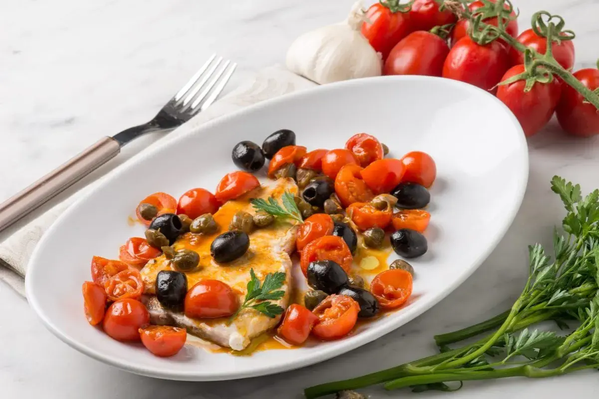 Piatto di pesce spada con pomodorini, olive nere e capperi. Una ricetta mediterranea gustosa e colorata.