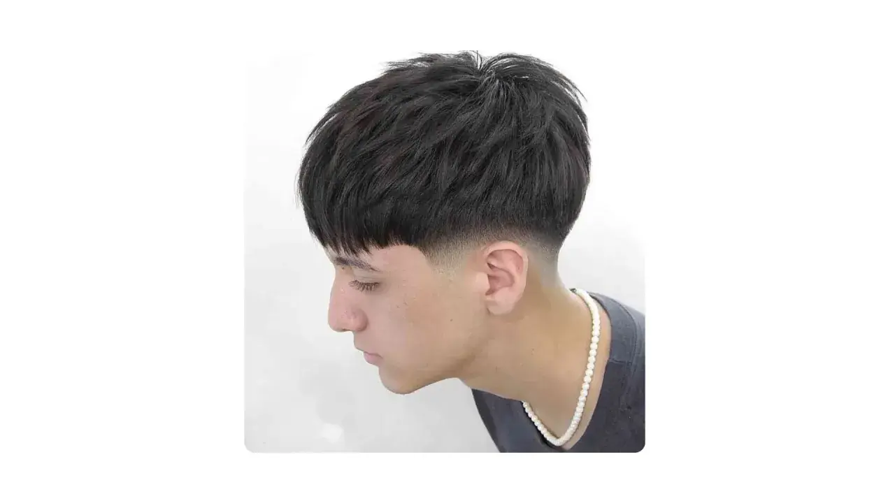 Joven con corte de pelo moderno, con flequillo recto y un degradado bajo (low fade) en los laterales.