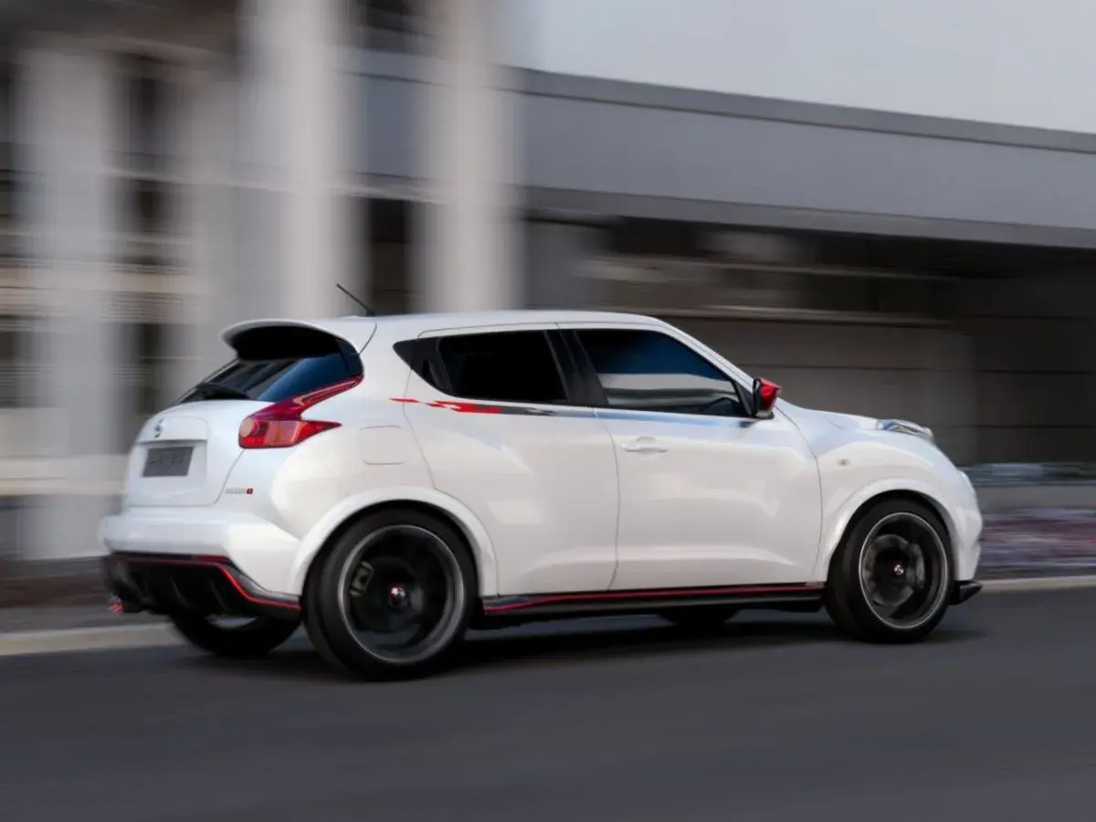 Biały Nissan Juke 1.5 dCi w wersji Nismo, z czerwonymi akcentami, pędzi ulicą. Jego sportowy wygląd budzi pozytywne opinie.