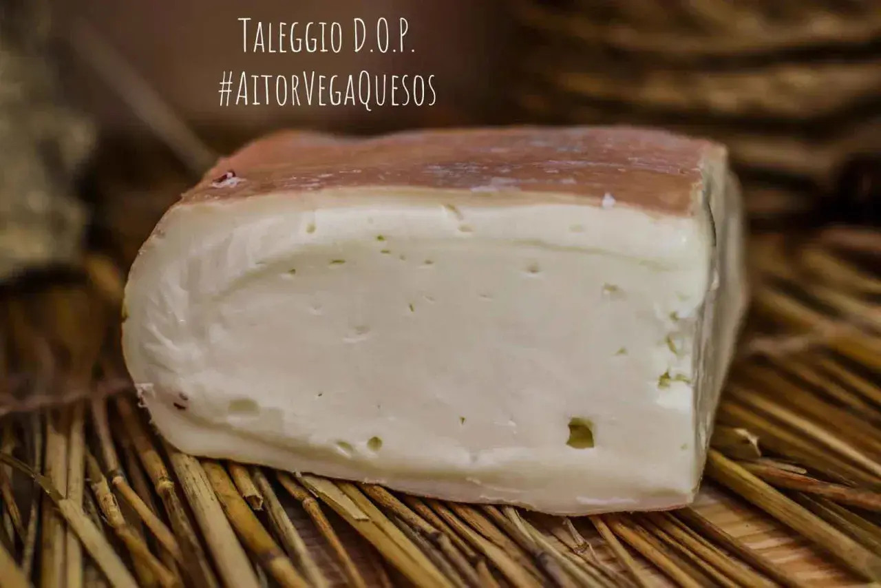 Un trozo de queso Taleggio D.O.P. con corteza rosada y pasta blanca, sobre paja. El queso Taleggio es fuerte y delicioso.