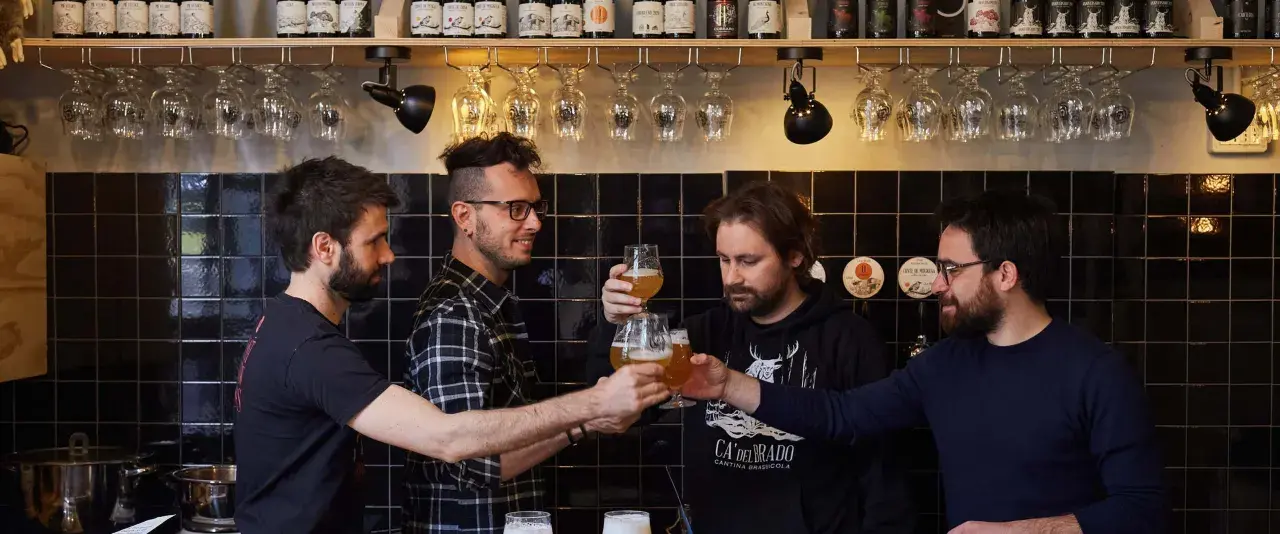 Amici brindano durante una visita birrificio. Bottiglie di birra e bicchieri in primo piano.