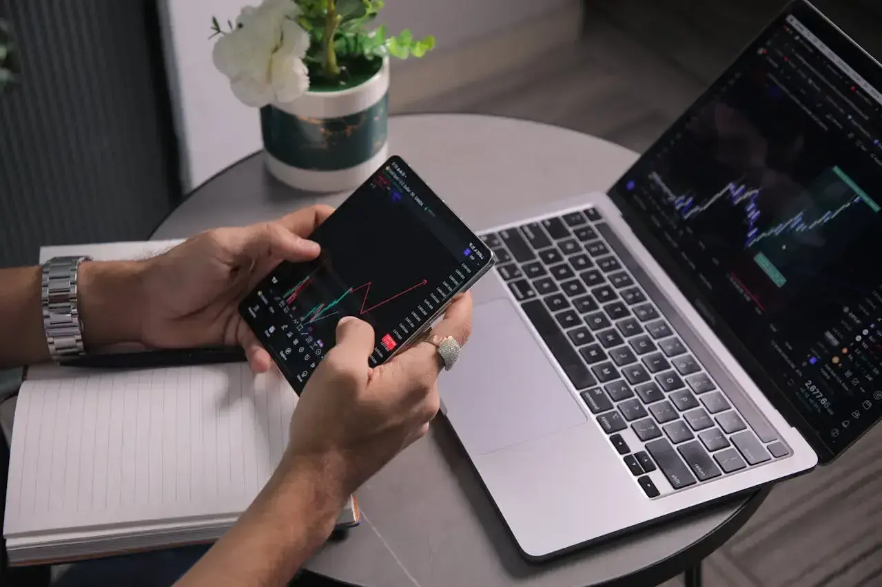 Analityk sprawdza wykresy na telefonie i laptopie, analizując dane finansowe.