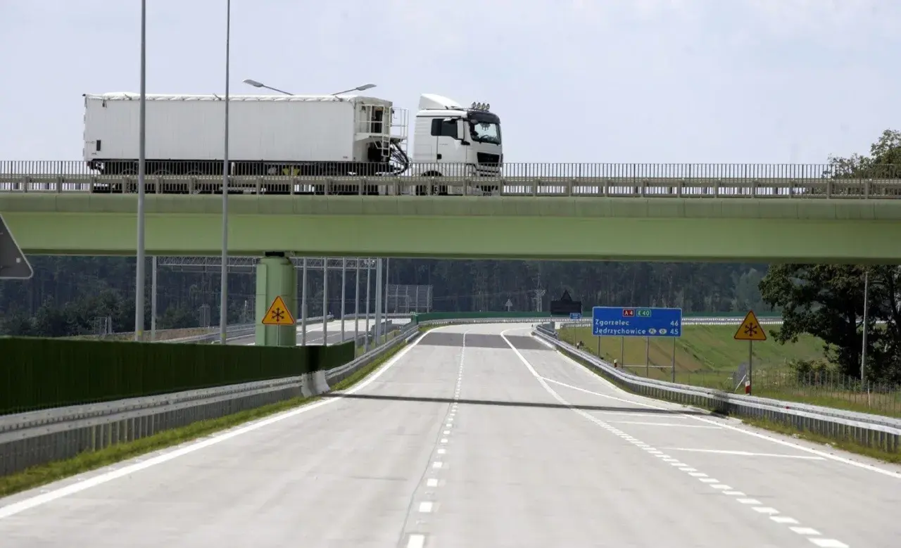 Ciężarówka na zielonym wiadukcie nad pustą autostradą z tablicami kierunkowymi.