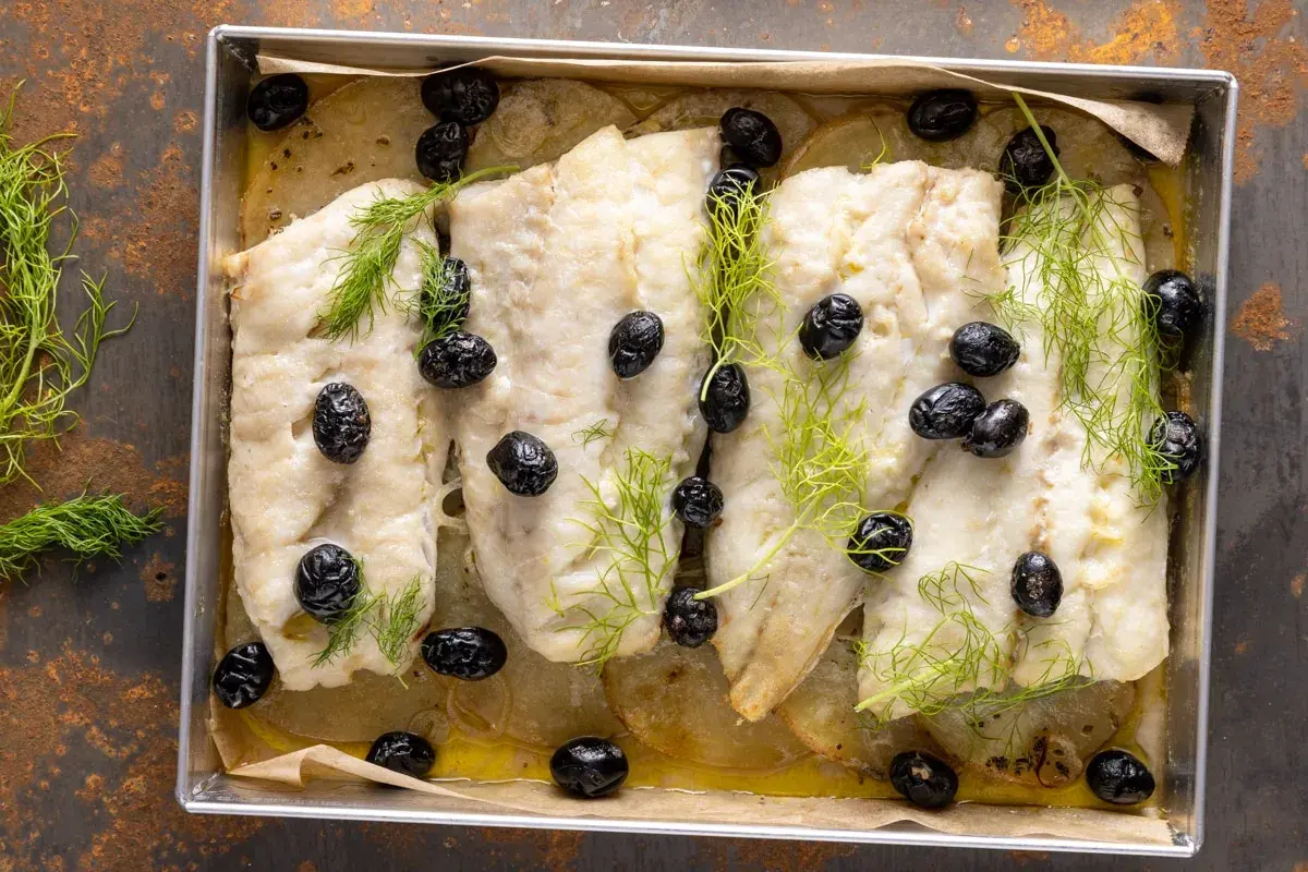 Merluzzo al forno con patate, olive nere e finocchietto fresco. Un piatto semplice e gustoso, pronto per essere servito.