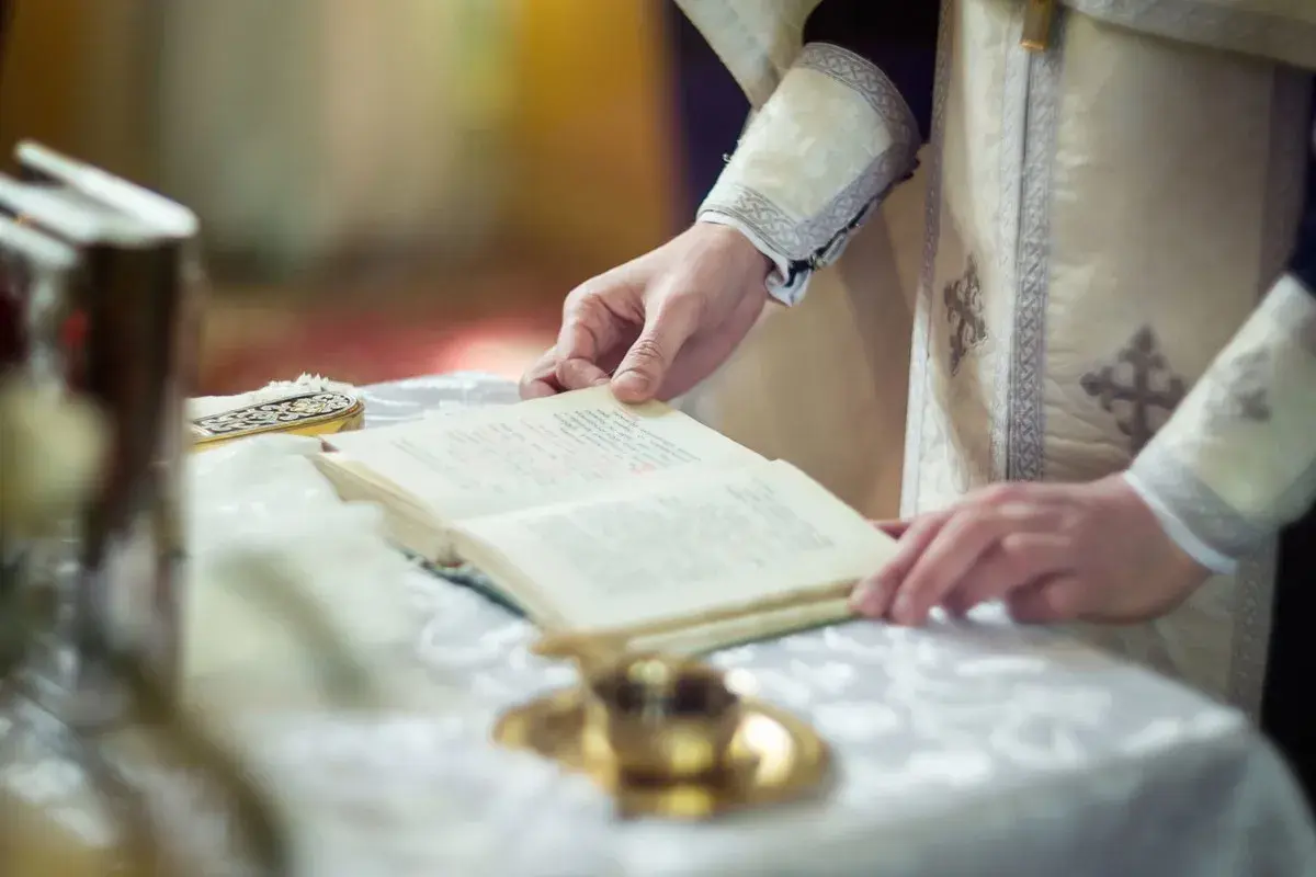 Dłoń duchownego trzyma księgę, czytając tekst. To może być fragment o tym, czym jest rezurekcja.