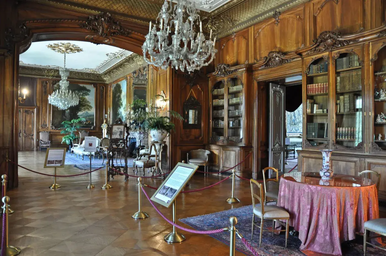 Eleganckie wnętrza Zamku w Pszczynie: kryształowe żyrandole, bogato zdobione boazerie, zabytkowe meble i biblioteka.