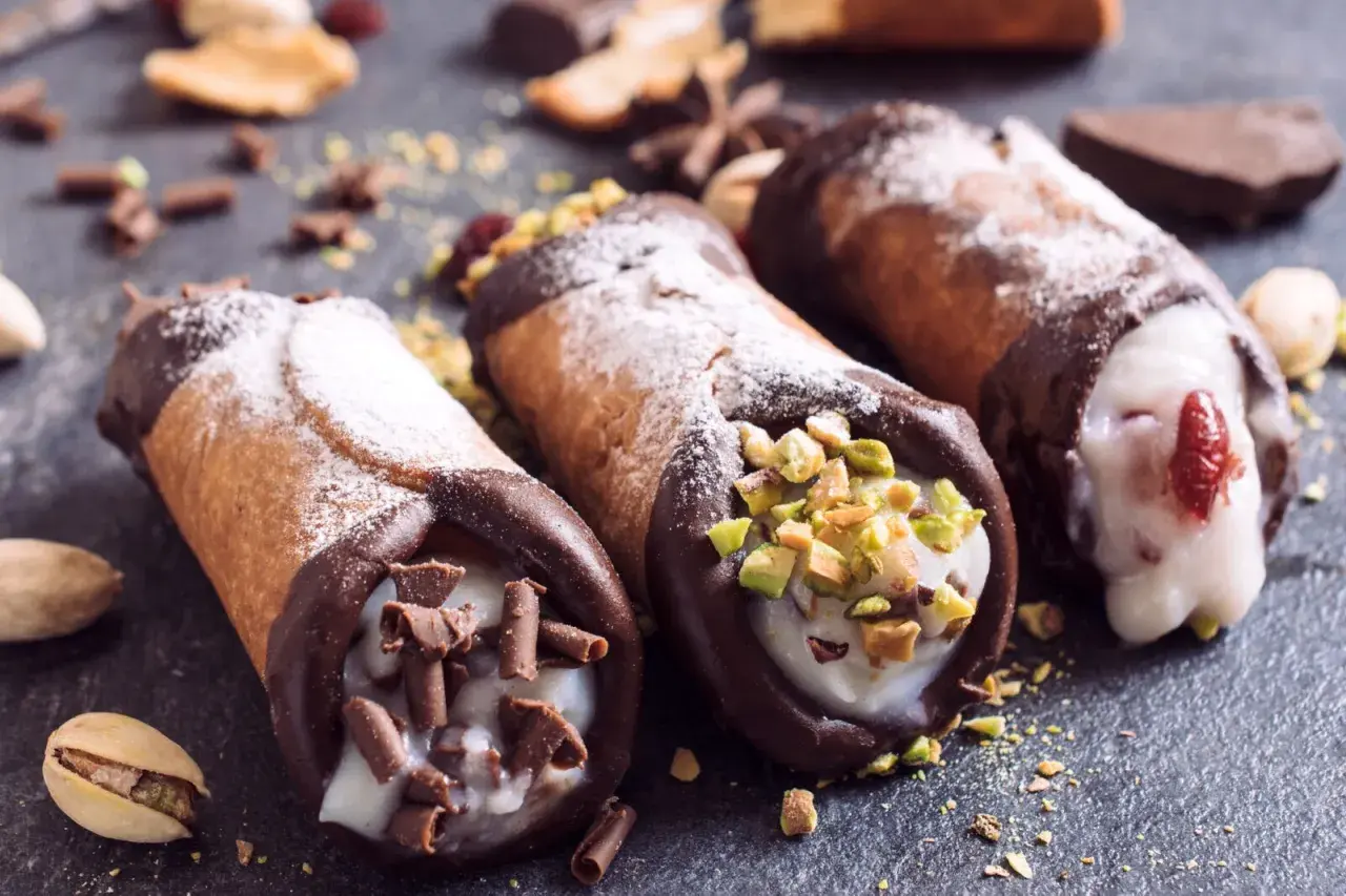 Trzy pyszne cannoli z kremem, posypane cukrem pudrem, pistacjami i czekoladą. Idealne na deser, gdy szukasz inspiracji na cannoli przepis.