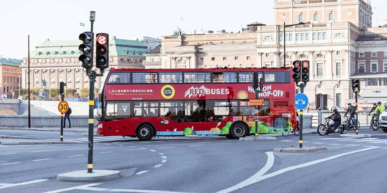 Röd dubbeldäckare för city sightseeing Stockholm passerar en korsning med trafikljus.