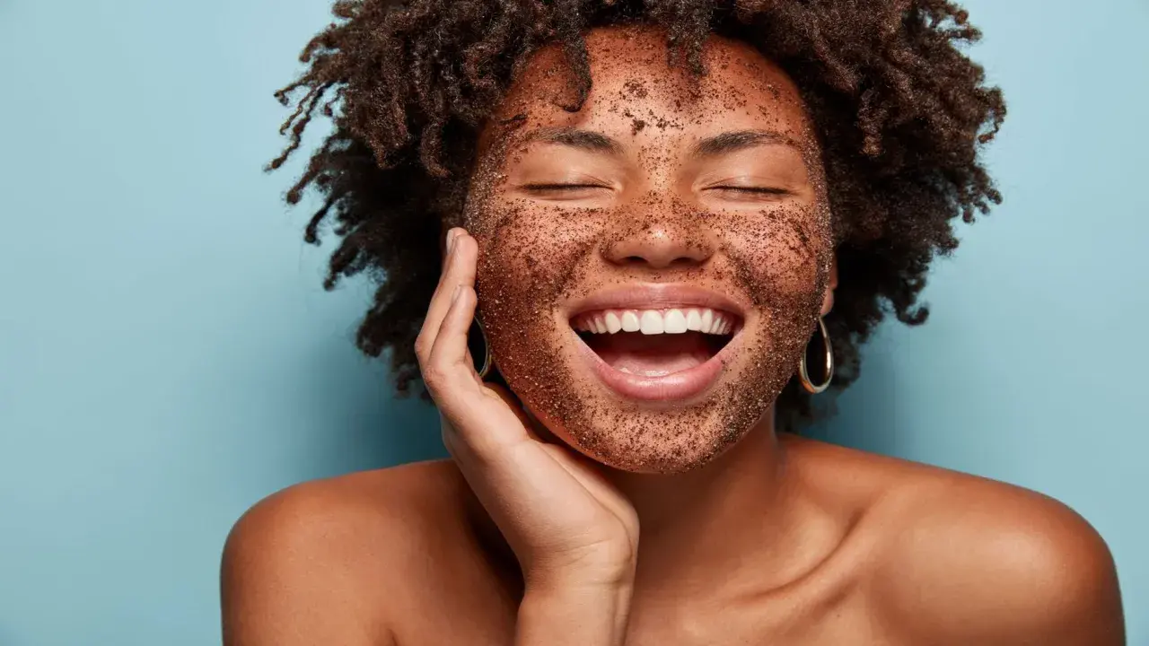 Mujer sonríe con la cara cubierta de exfoliante, mostrando cómo exfoliar la piel para un brillo radiante.