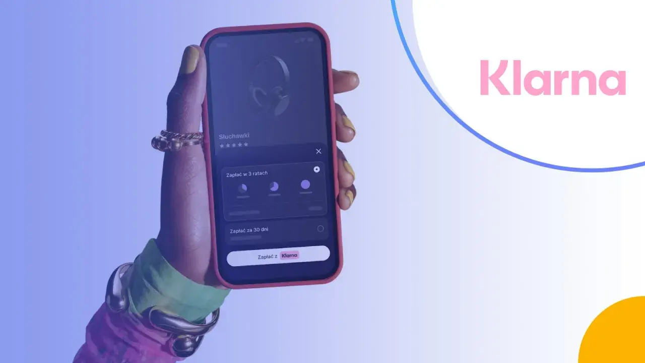 Dłoń trzyma smartfon z aplikacją Klarna, umożliwiającą zakup słuchawek na raty.