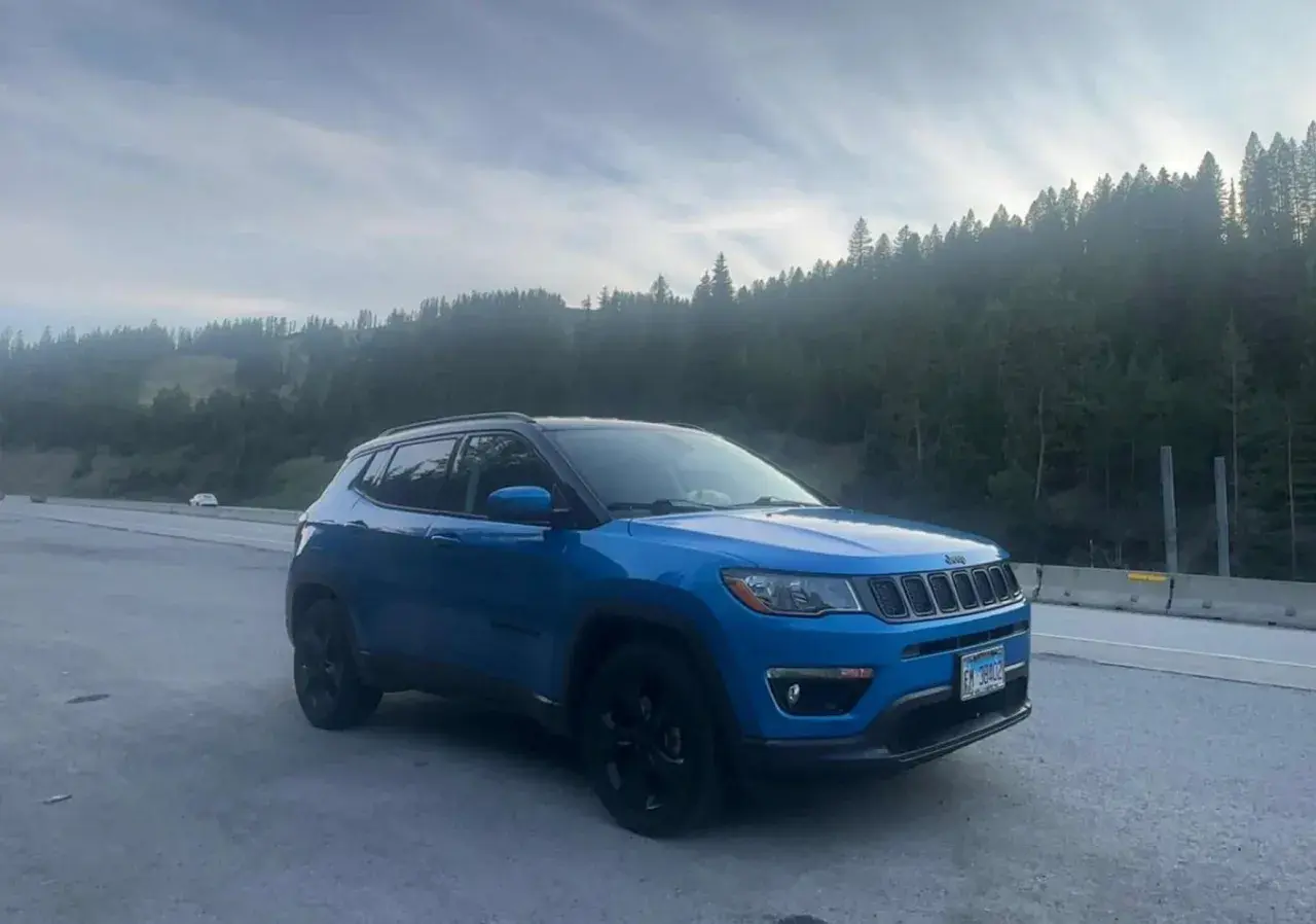 Blå Jeep Compass står vid vägkanten med en skog i bakgrunden. Kanske ett oväntat stopp, en Jeep Compass problem?