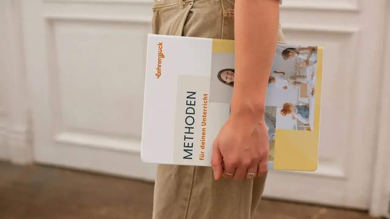 Ein Buch mit dem Titel "Methoden für deinen Unterricht" wird von einer Person gehalten. Es zeigt Bilder von Kindern in einer Lernumgebung.