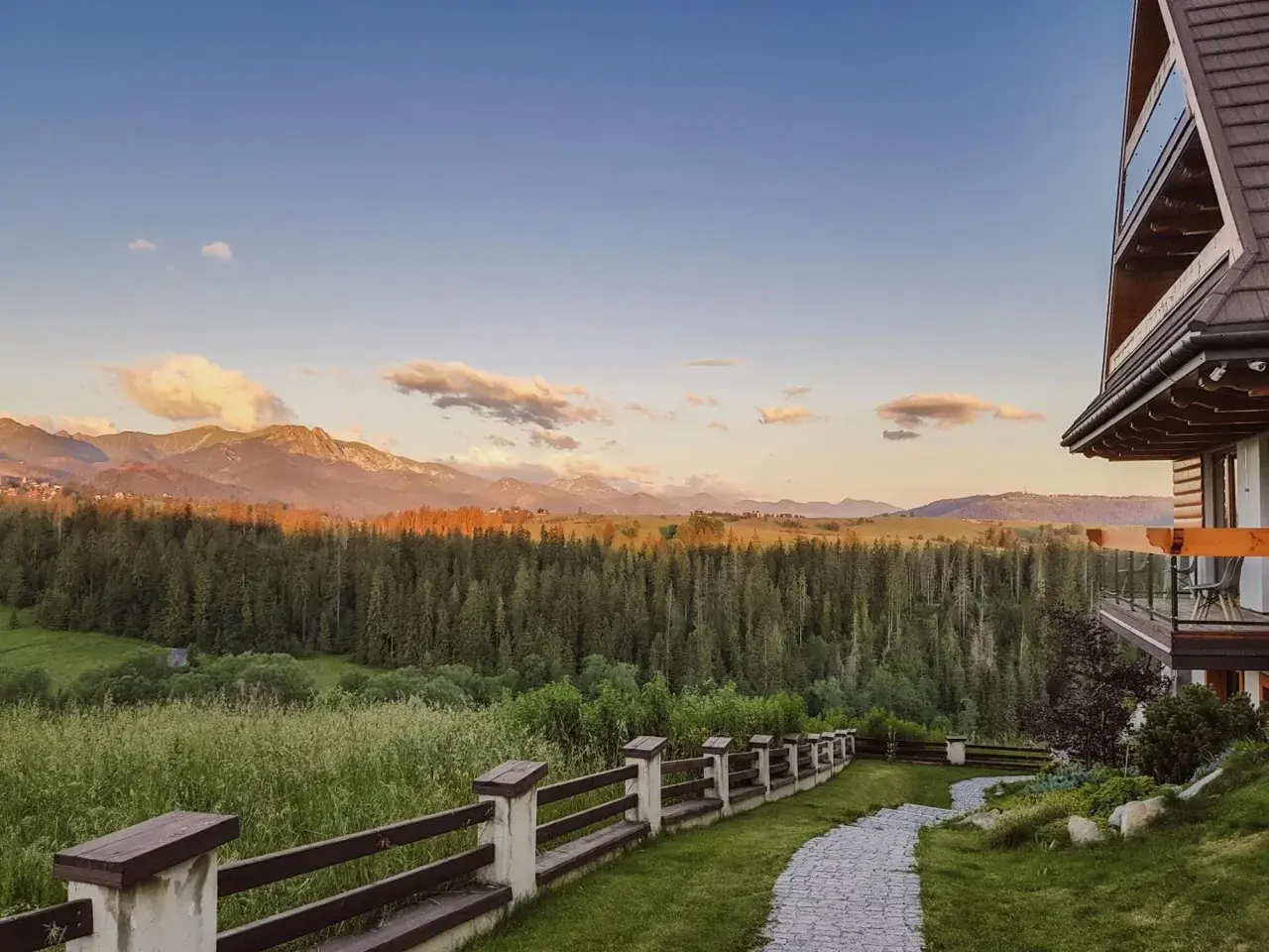 Widok z hotelu Kopieniec Murzasichle na Tatry o zachodzie słońca. Drewniany domek, kamienna ścieżka i las.
