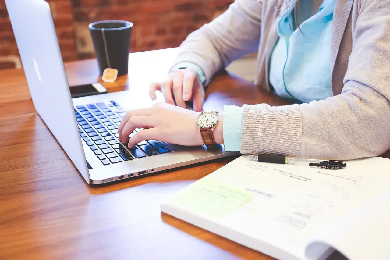 Kobieta pracuje na laptopie, obok notatnik i kubek z herbatą. Czyżby przygotowywała dokumenty dotyczące redukcji etatu i umowy na czas nieokreślony?