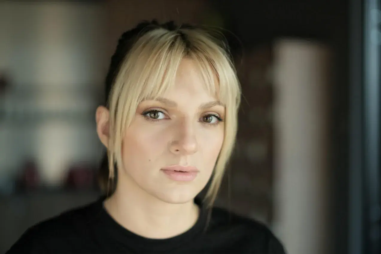 Portret młodej kobiety z blond grzywką i ciemnymi pasemkami włosów, patrzącej w obiektyw.