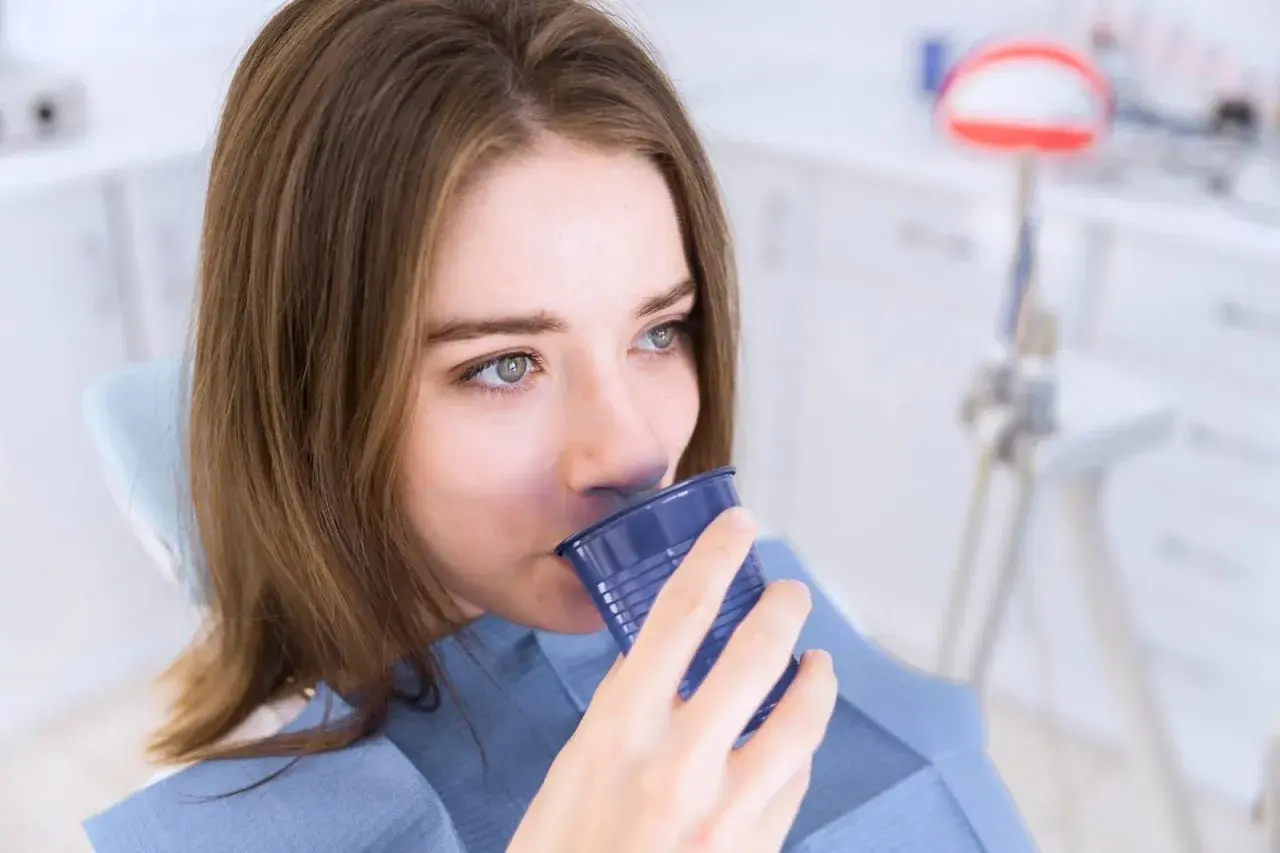 Ragazza in poltrona dentistica beve da un bicchierino blu, forse dopo un trattamento con clorexidina cos'è.