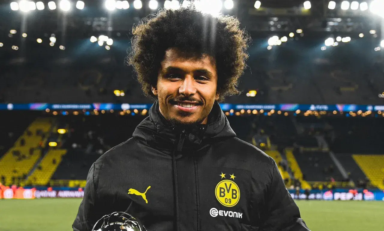 Karim Adeyemi z BVB z pucharem, uśmiecha się na tle stadionu.