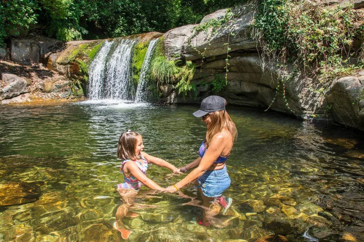 Madre e hija disfrutan de unas refrescantes piscinas naturales con una cascada al fondo.