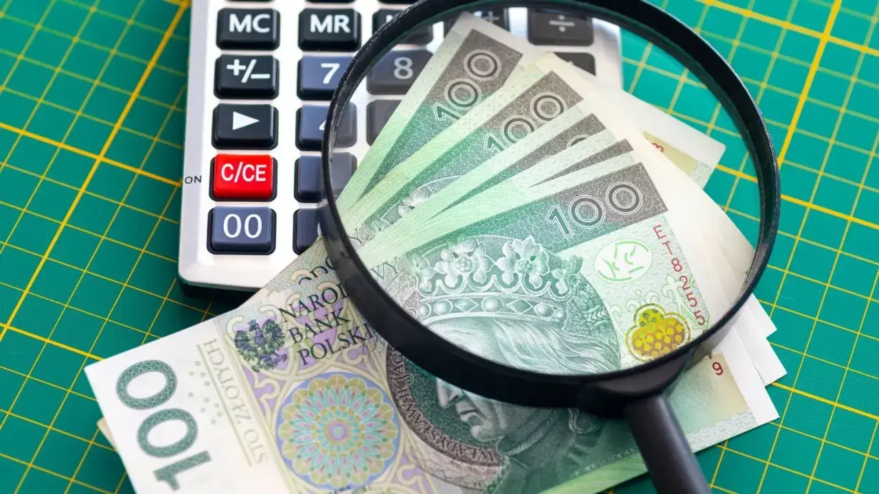 Kalkulator, lupa i polskie banknoty 100 zł na zielonym tle.