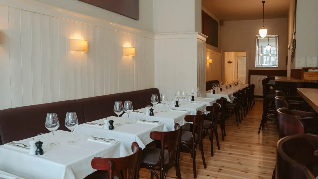 Elegantes Restaurant in Berlin, bereit für Gäste. Tische sind mit weißen Tischdecken, Gläsern und Besteck gedeckt. Gemütliche Atmosphäre dank Wandlampen.