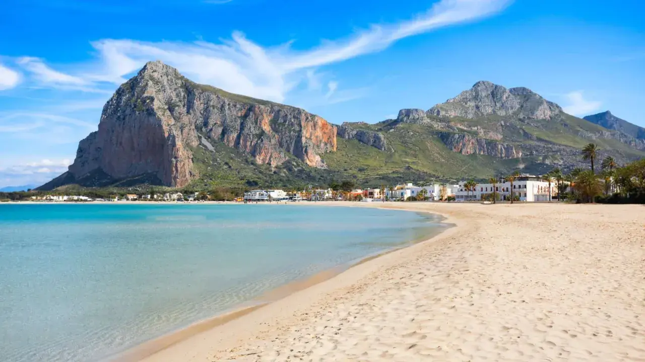 Spiaggia di San Vito Lo Capo, Sicilia, con acque turchesi e montagne imponenti sullo sfondo. Un paradiso per chi ama il mare.